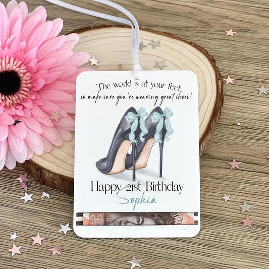 Acrylic money holder featuring the image of a pair of high heeled shoes with a blue bow on the back of the shoes and the text ' The World is at your feet, so make sure you're wearing great shoes! Happy 21st Birthday Sophia. This can be personalised with any name and age.